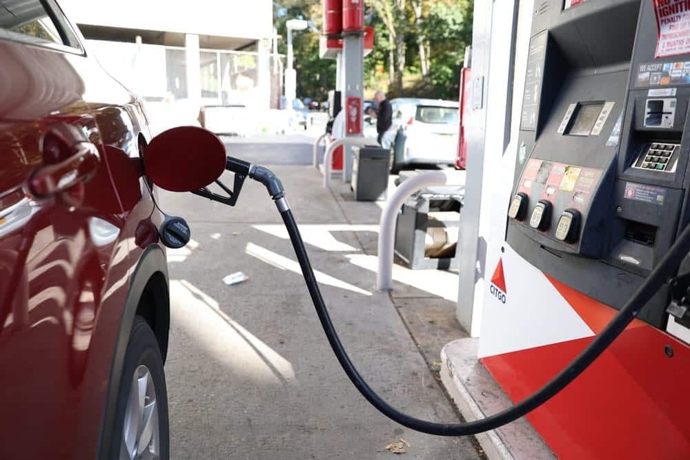A red car in the US is filling up at a gas station while analysts monitor gas prices.