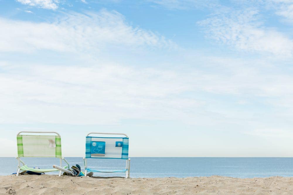 Two beach chairs sit on the sandy shore at the Bolivar Beach Club, open to RV Resort guests and offering stunning ocean views.