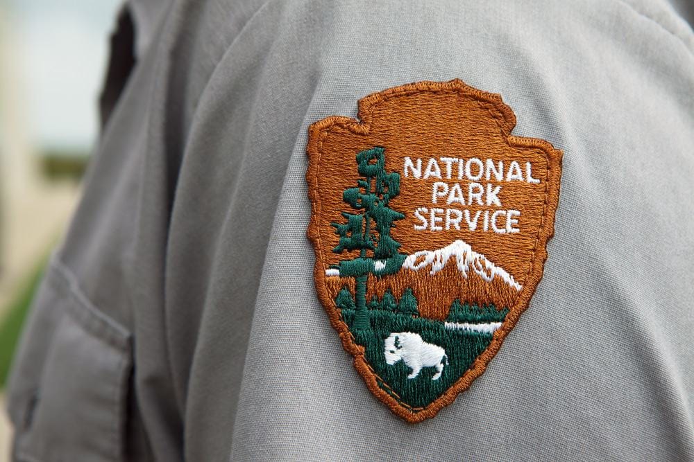 A man proudly wears a National Park Service badge on his jacket.