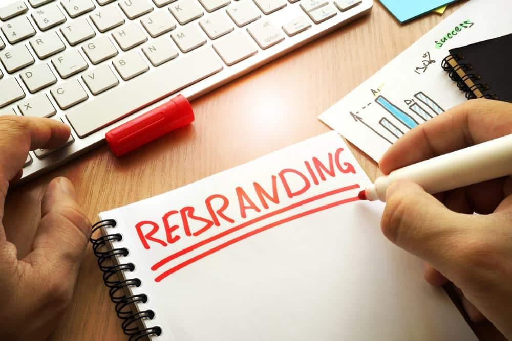 A hand writing the word rebranding on a notebook.