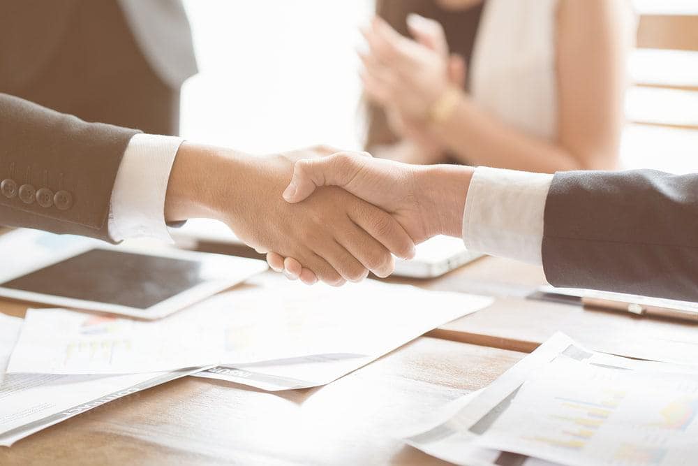 Two business people shaking hands over a table during an acquisition deal at a RV dealership.