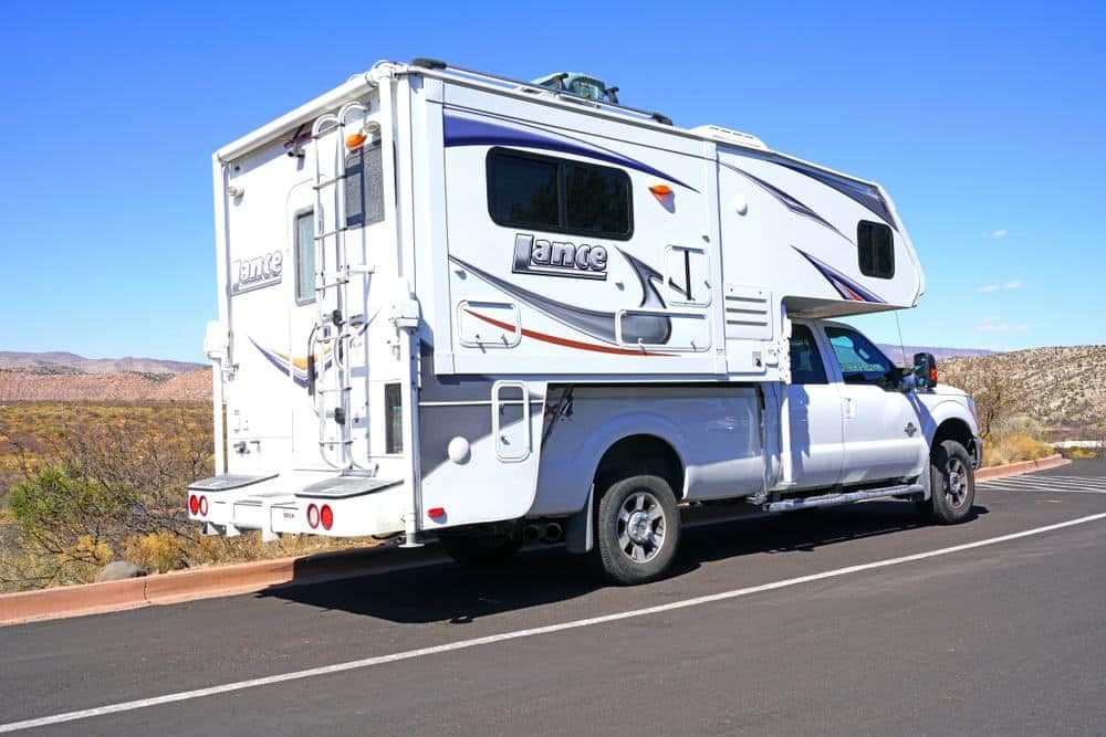 A white RV, owned by an RV owner or truck camper owner, parked on the side of the road.