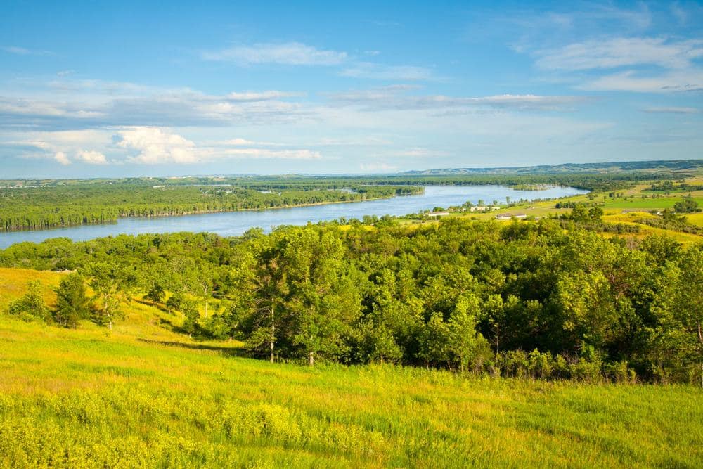A picturesque view of a river and a lush green field in one of North Dakota State Parks, enhanced by recent infra upgrades supported by pandemic funds.