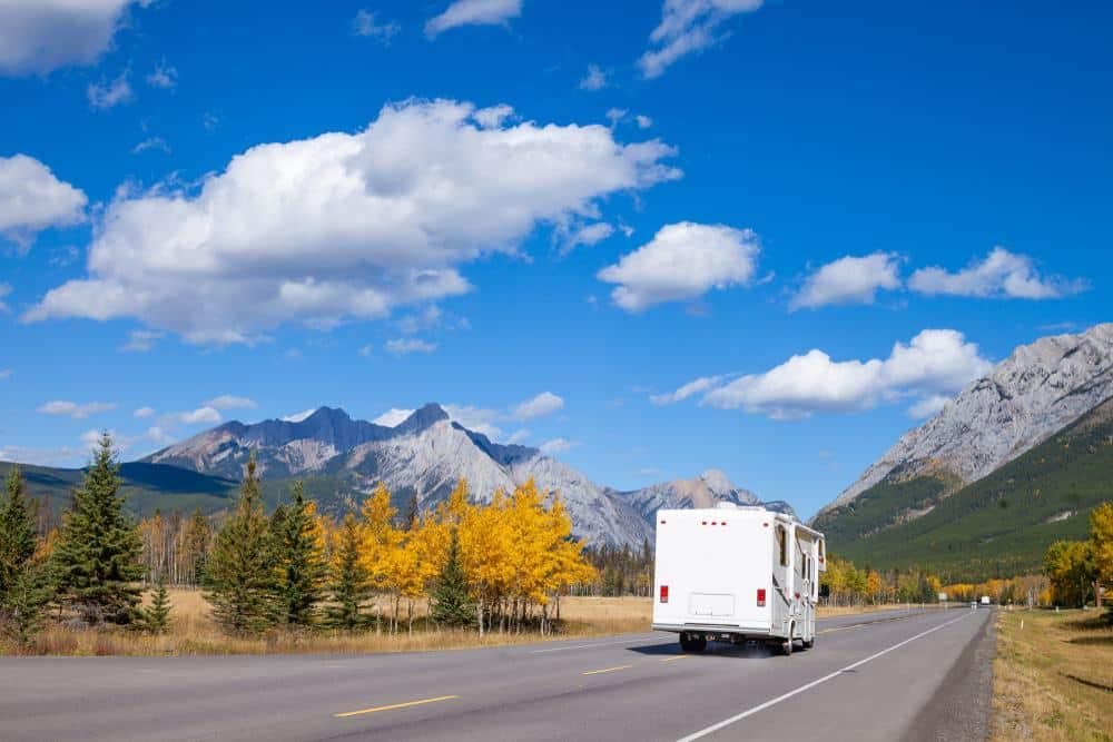 An RV park owners traveling down a road with mountains in the background.