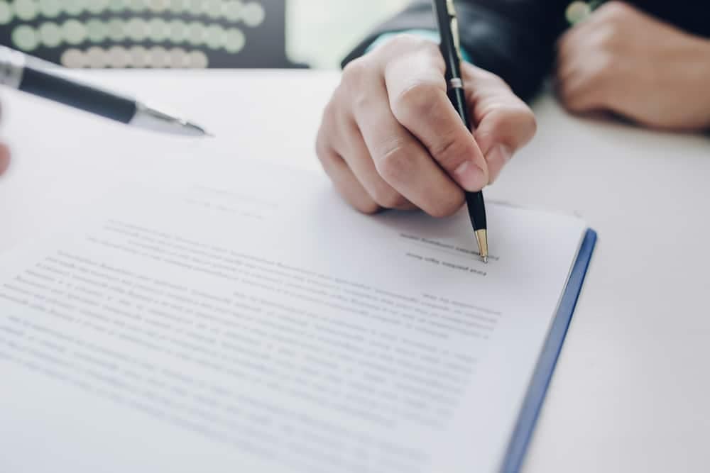 A person signing a document with a pen.