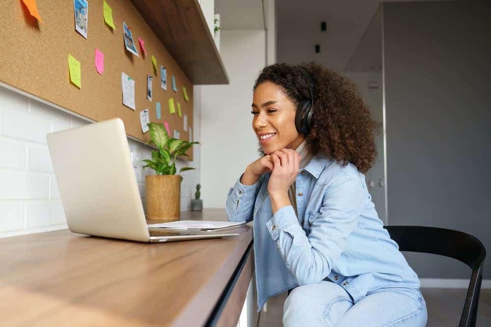 A woman wearing headphones is sitting at a desk using a laptop while attending a BCLCA webinar, operating in 2022.