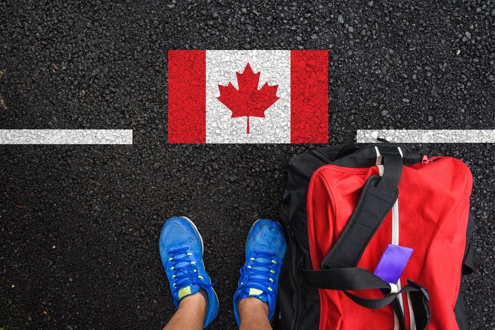A Canadian flag and a red suitcase on a road, symbolizing the journey of vaccinated travelers amidst COVID-19 testing.