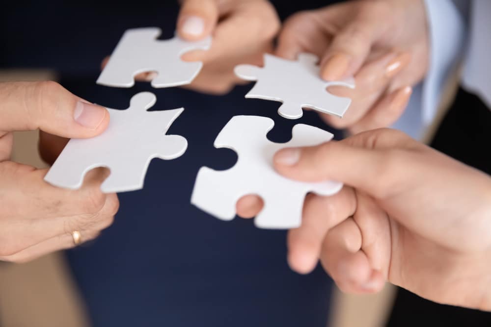 A group of business people holding a puzzle piece together, symbolizing the collaboration and unity within AL-KO Vehicle Technology and DexKo Group.