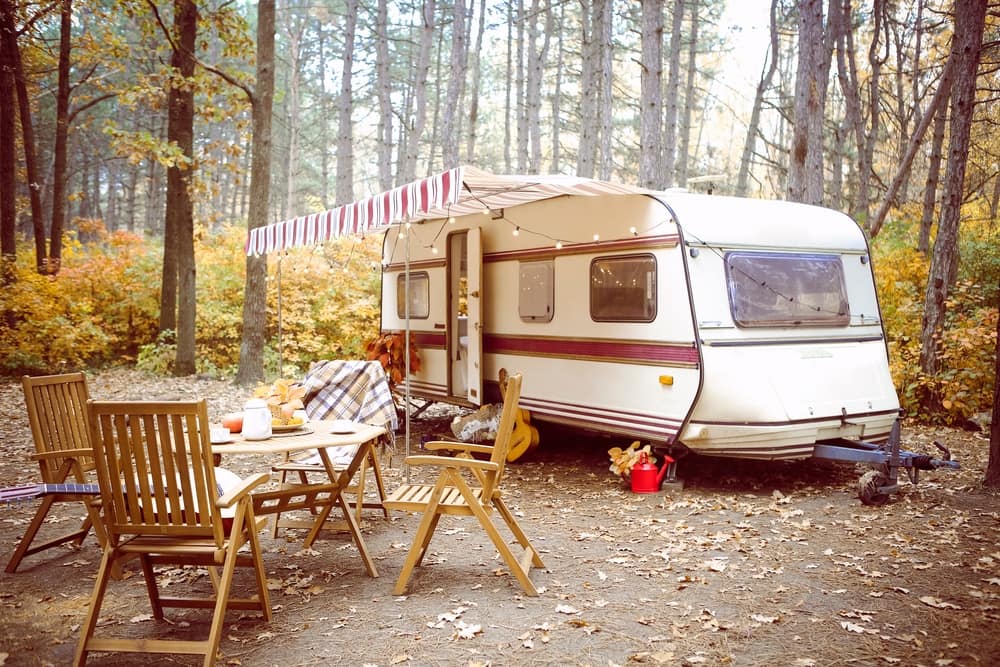 A caravan parked in the woods with a table and chairs, offering a surge of tranquility amidst the serene landscapes of Wales.