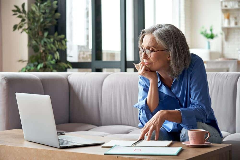 A woman is sitting on a couch participating in a CCRVC conference while looking at her laptop.