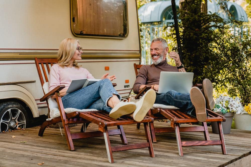 A couple sitting in lawn chairs with laptops in front of an RV making Florida travel reservations.