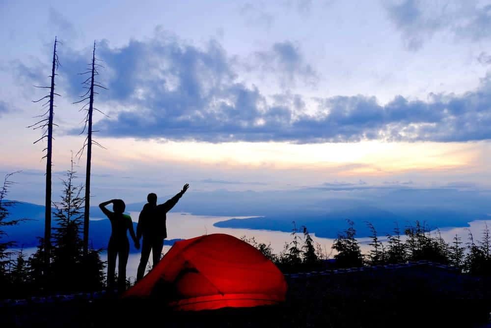 Two outdoor enthusiasts standing in front of a tent on top of a mountain.