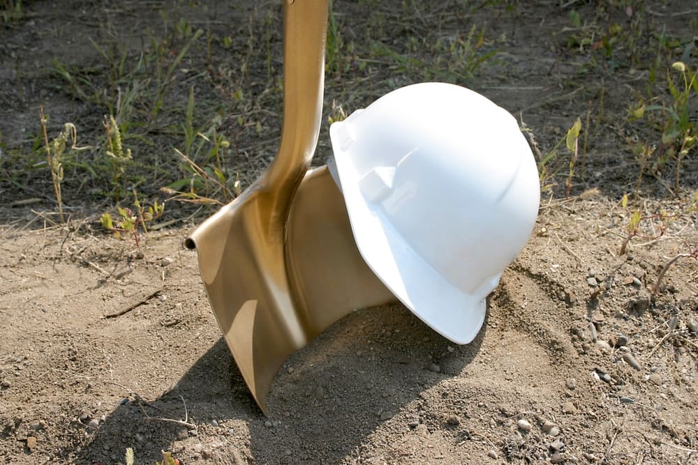 A white hard hat with a shovel in the dirt.
