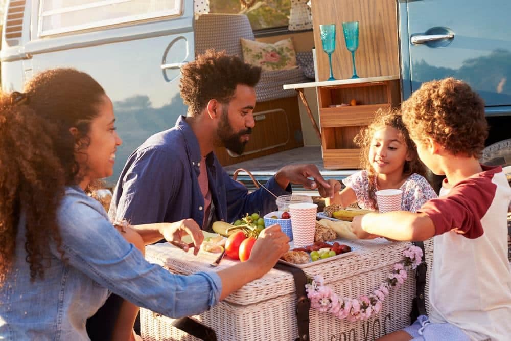 Black Folks Camp Too - A family enojying a picnic in front of a VW camper van.