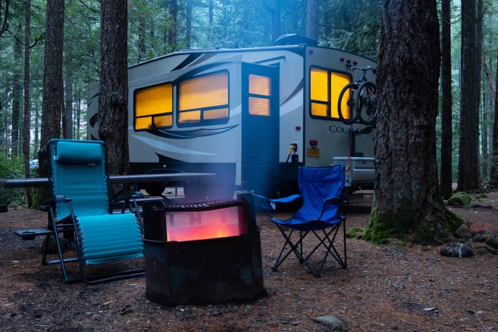An RV parked in a park with a fire pit.