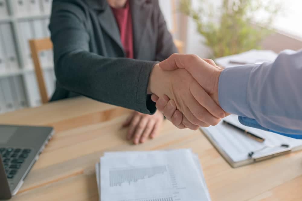 Two business people from Jacobs Vehicle Systems and Cummins shaking hands at a desk after an acquisition.
