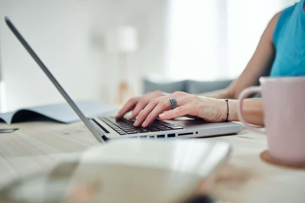 A woman typing on a laptop while enjoying a cup of coffee, working on the launch of BCLCA's new corporate site.