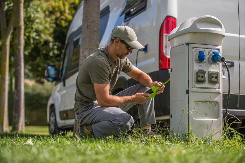A man wearing a hat is working on a generator in front of an RV, incorporating clean technologies.