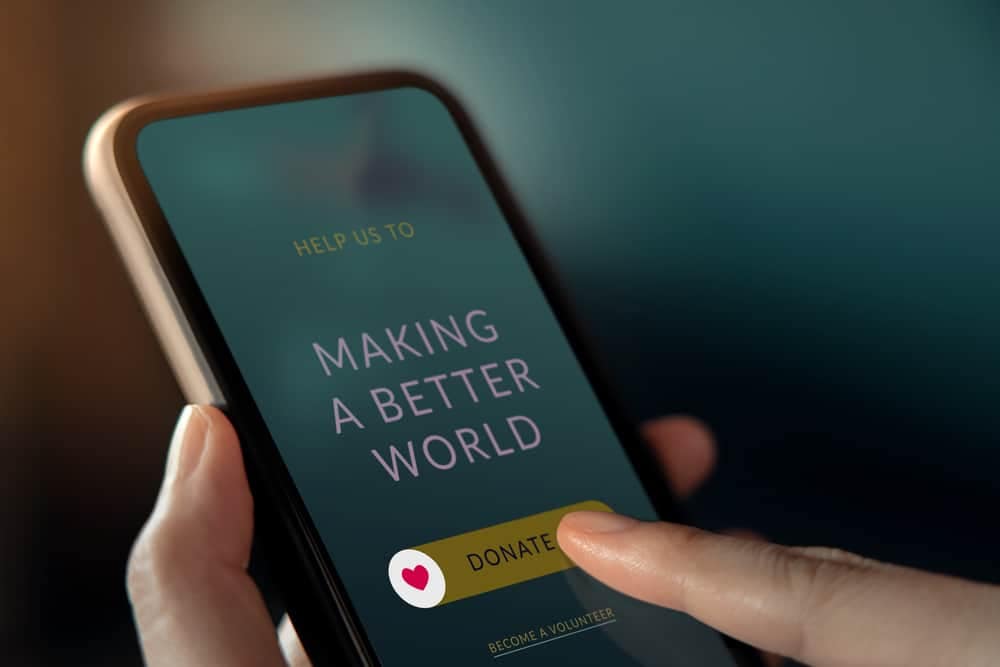 A hand holding a smartphone with a fundraiser button on it.