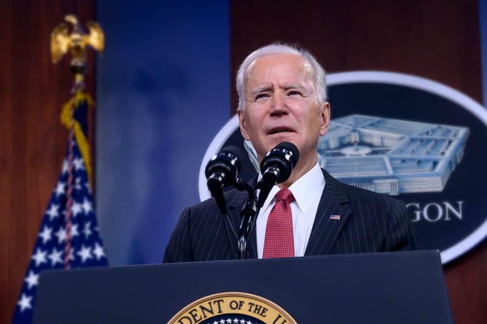 President Joe Biden speaks at a podium in front of an American flag while addressing the importance of protecting America's forests through an executive order.