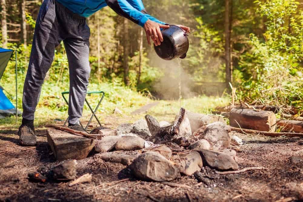 An adventurer is cooking over a campfire in the woods, following the Camper's Code to responsibly enjoy nature.