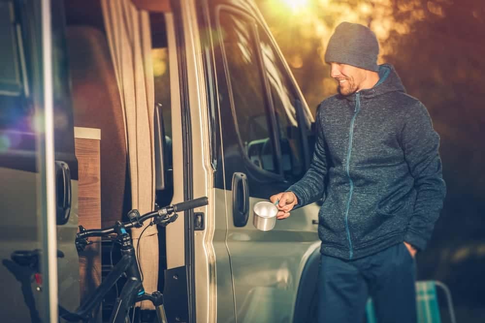 A man is standing next to a camper van with a cup of coffee, enjoying the convenience of the cup holders.