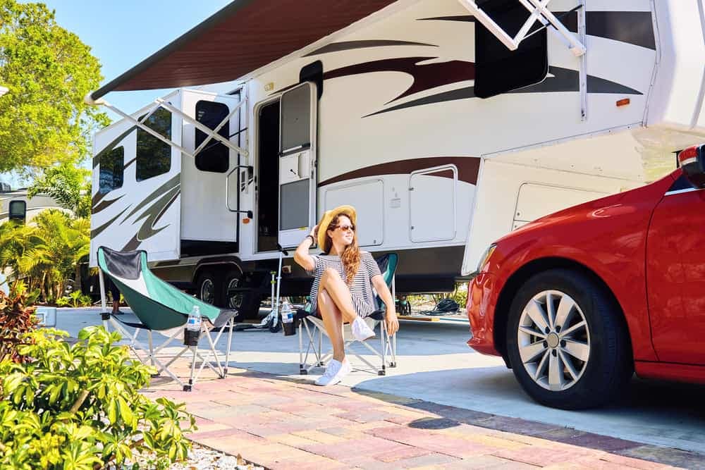 An expensive woman enjoys her booming RV rental, sitting in front of a red car.
