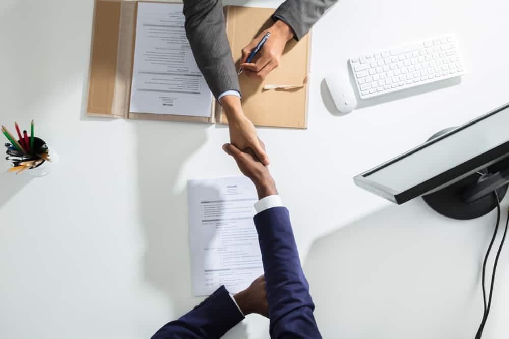 Two business people from the REV Recreation Group shaking hands at a desk.