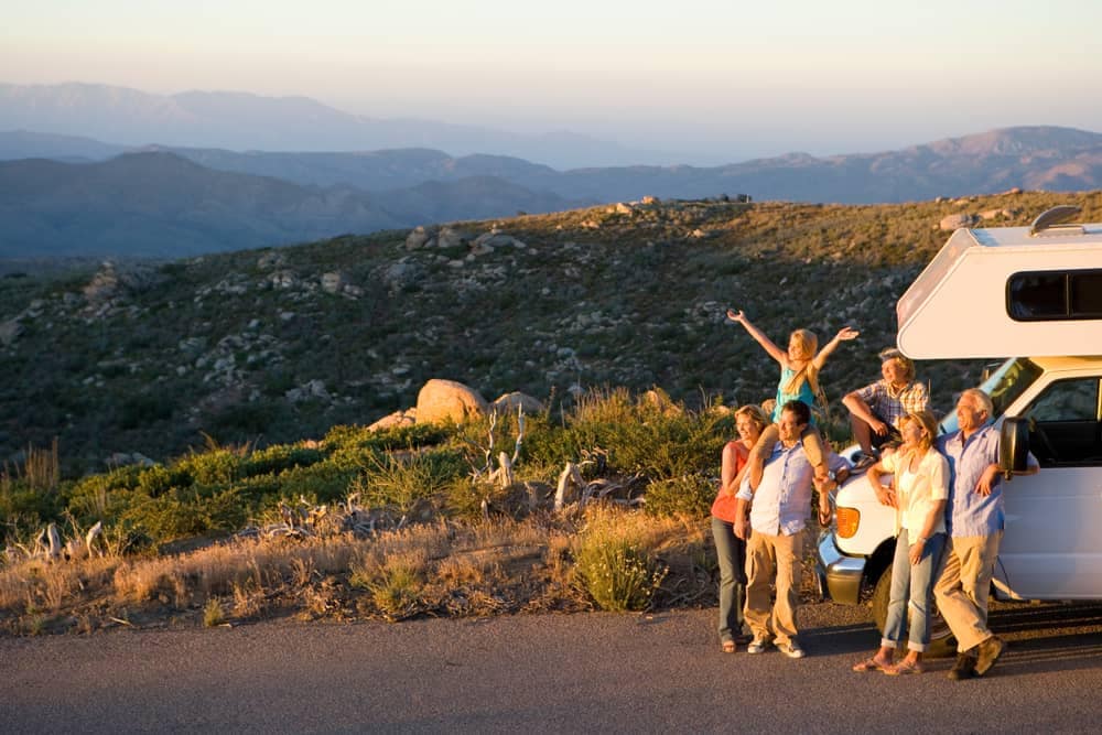 A group of people standing in front of an RV retailer with mountains in the background.