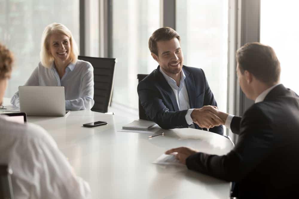 A group of business people shaking hands at a Camping World dealership acquisition meeting.