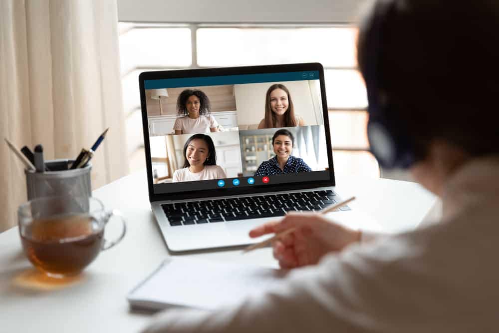 A woman using a laptop during a video call with a group of people.
