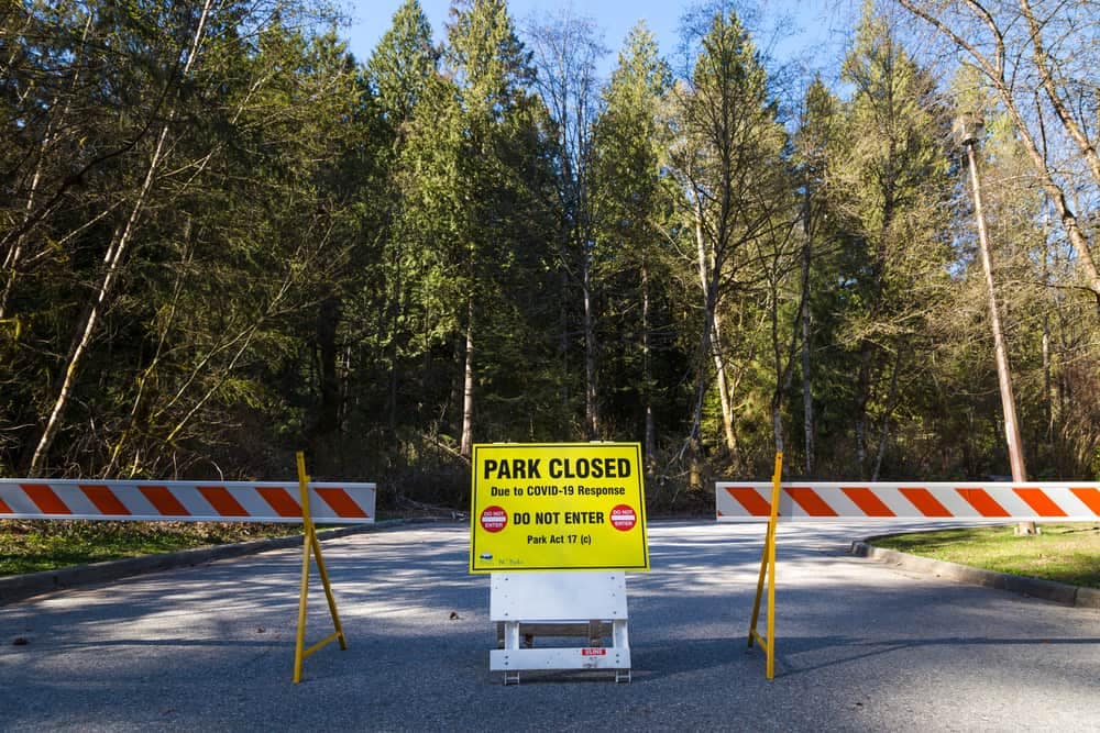 A park closed sign sits in the middle of a forest.
