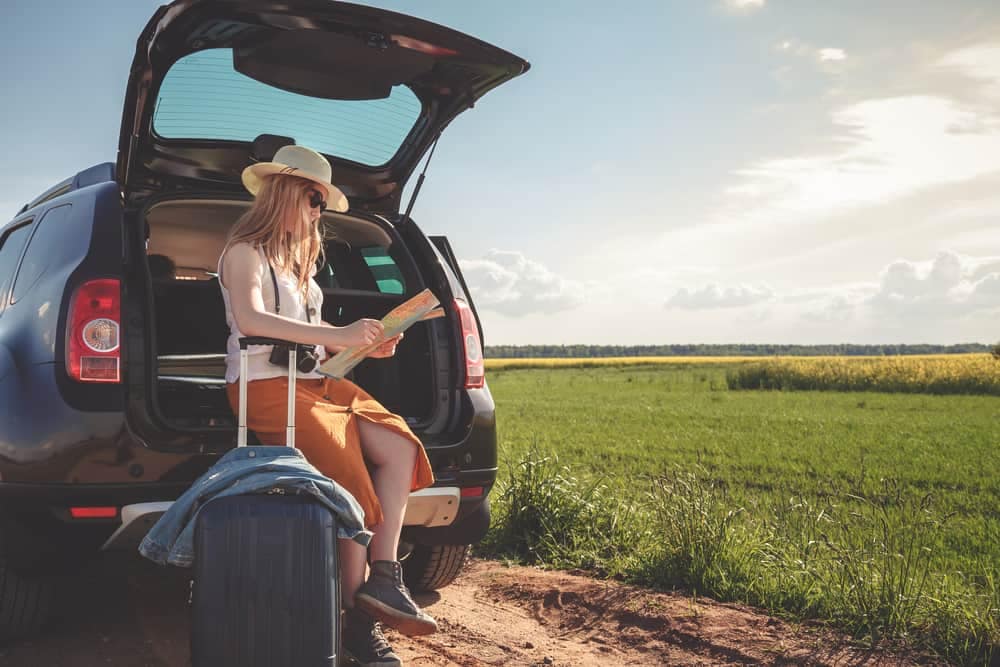 A Gen Z woman sitting in the back seat of an SUV with a map in her hand, embarking on an unplugging campcation.