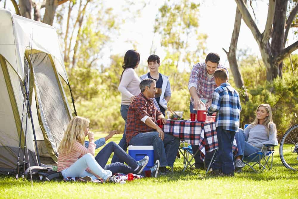 A group of people sitting around a campfire near a tent, engaged in exciting Memorial Day activities.