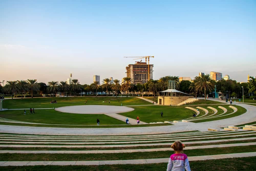 A young girl is standing in front of a green grassy area, enjoying the outdoor recreation.