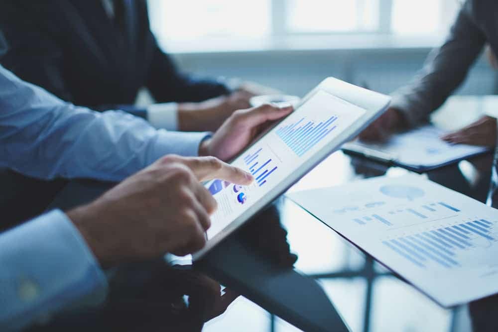 A group of business people analyzing graphs on a tablet to strategize for increased revenue in Q4 2021.