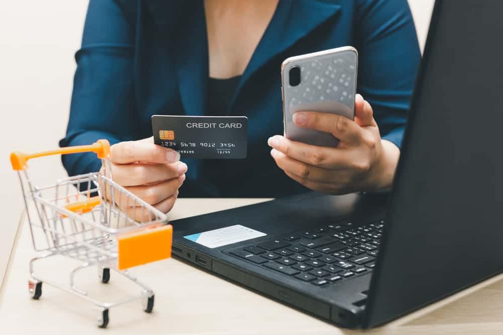 A woman utilizing a laptop for online shopping, with a credit card in hand.