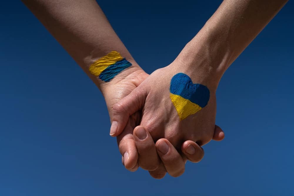 Two Ukrainian refugees holding hands painted with the flag of Ukraine.