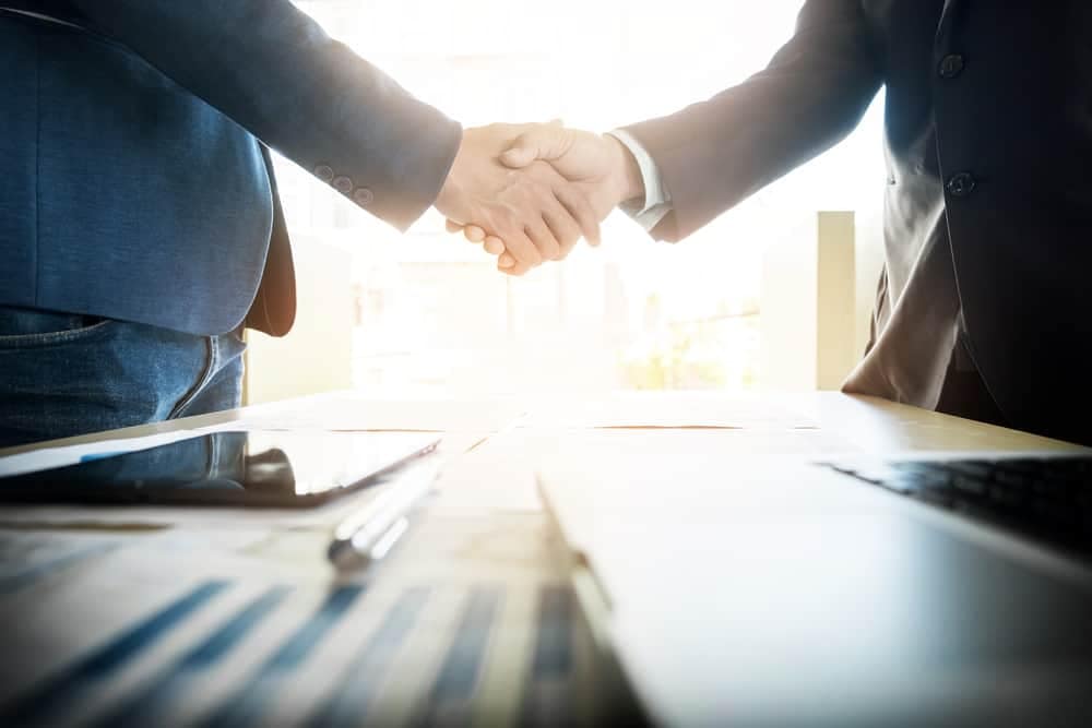 Two businessmen shaking hands in front of a desk.