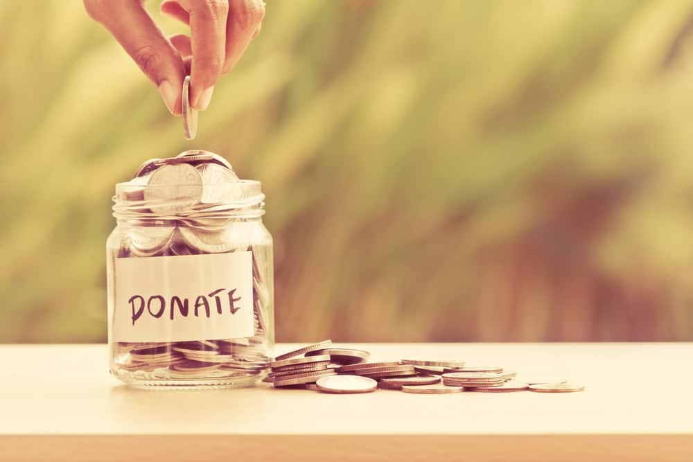 A hand putting coins into a jar labeled "donate" as part of a retailer's campaign.