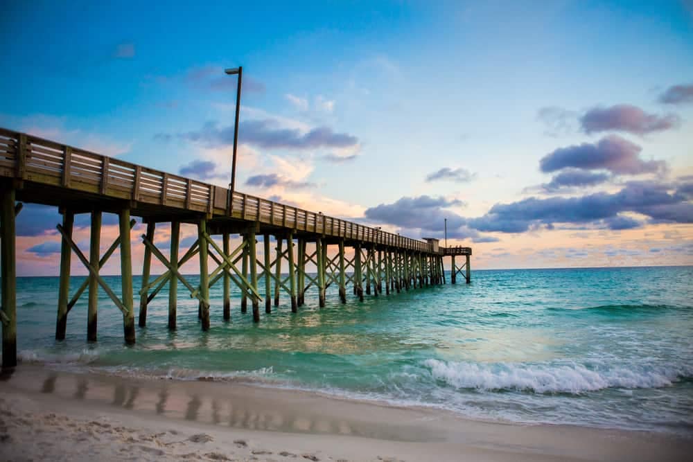 A pier at St. Andrews State Park with waves crashing on the beach at sunset.