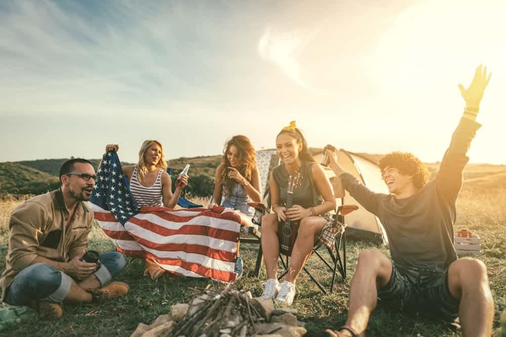 A group of friends sitting around a campfire on the Fourth of July with an American flag.