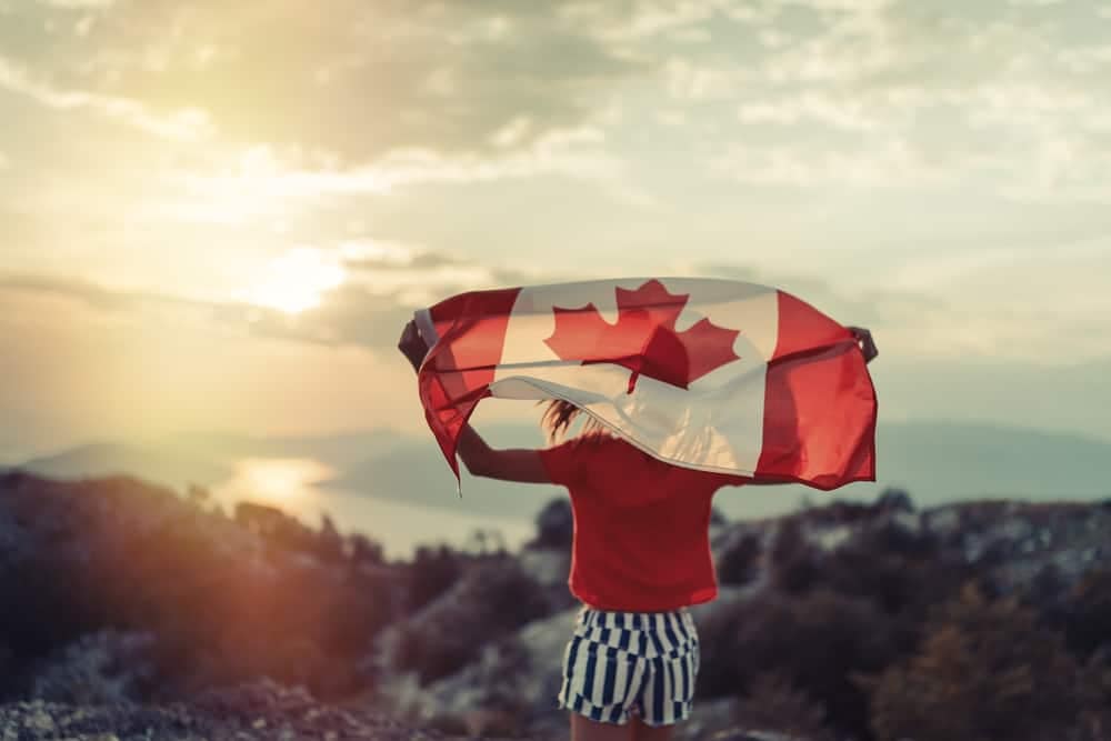 A Canadian woman proudly waving the Canadian flag atop a majestic mountain peak during her travel excursion.