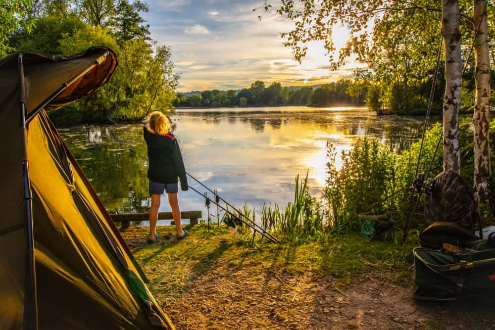 A woman is standing next to a tent on a lake.