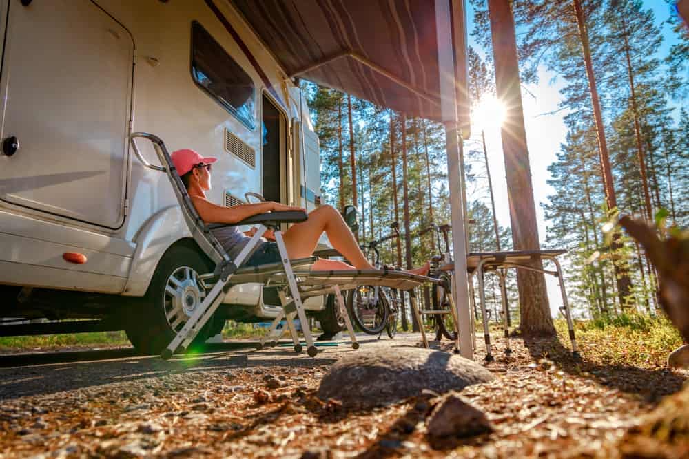 A woman relaxes in front of her First Camper Trailer in the woods.