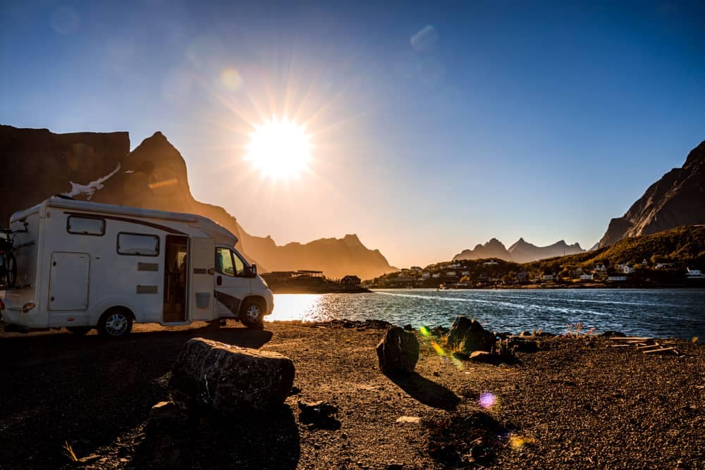 An Australian caravan parked in front of a lake with mountains in the background.