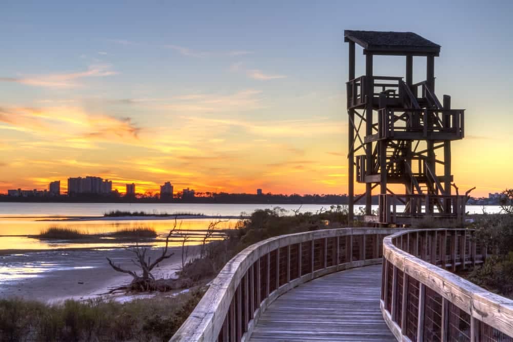 A boardwalk leading to a beach with a lighthouse in the background, accessible for Library Card Holders.