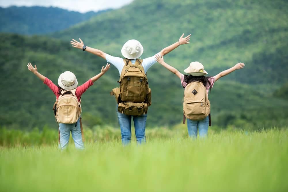 Three children with backpacks standing in a field with mountains in the background, promoting Boost Tourism.