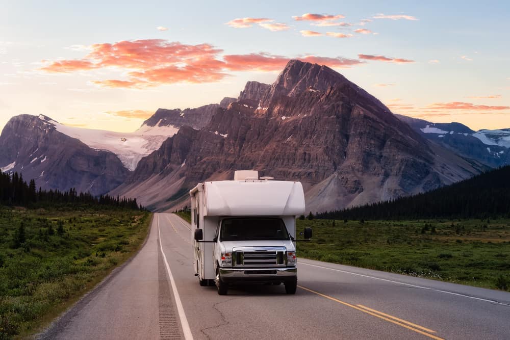 A white rv driving down a road with mountains in the background, showcasing Kerala's scenic beauty as part of a Caravan Tourism marketing campaign.