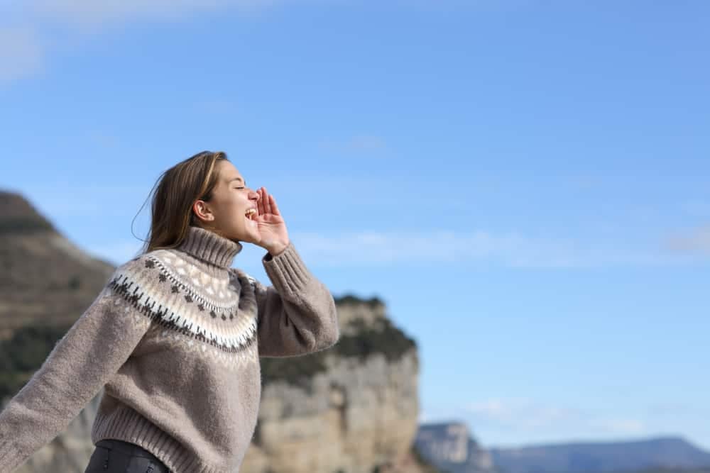 A woman is standing outside and blowing her nose in front of a cliff.